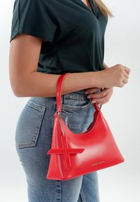 Bolsa tote sintética roja con forma curva, que presenta un acento cruzado prominente y un detalle de cadena en el asa. Acabado texturizado.