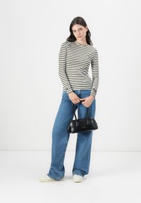 Long-sleeve striped top in olive and white, paired with blue wide-leg jeans and a small black handbag. White sneakers complete the look.