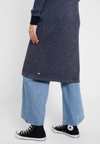 Marinblå ribbad stickad klänning med långa ärmar, sidoklyfta, ihop med ljusblå vida jeans och svarta högstövlar.