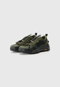 Grønne atletiske joggesko laget av teksturert stoff med svarte accenter, med en robust såle og en distinkt gul Vibram-logo.