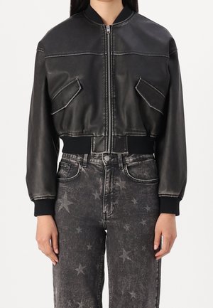 Veste en cuir noire courte avec fermeture éclair à l'avant et poches à rabat inclinées, associée à un jean noir taille haute avec un motif étoile délavé.
