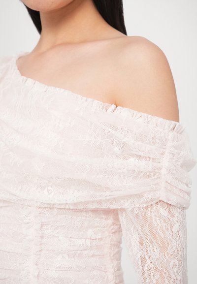 Koronkowa sukienka w delikatnym różowym kolorze z dekoltem odkrywającym ramiona. Posiada marszczenia, teksturowane kwiatowe wzory oraz przezroczyste koronkowe akcenty na rękawach.
