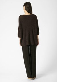 Pull en maille marron au fit ample, avec un col large et des manches trois-quarts, associé à un pantalon noir à jambes larges et des escarpins.
