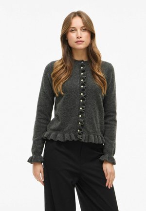 Tamsiai pilkas megztinis su raukšlėmis, mygtukų užsegimas ir ilgos rankovės. Turi apvalų kaklą ir minkštą tekstūrą.