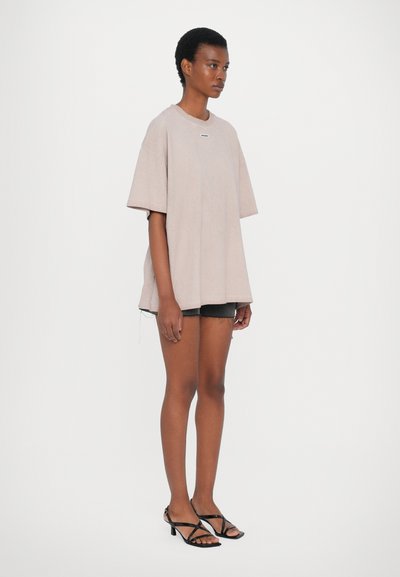 Oversized light beige t-shirt with a round neckline and short sleeves, paired with black denim shorts and black strappy sandals.