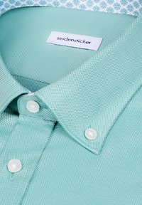 Chemise boutonnée texturée vert clair avec des boutons blancs et une étiquette blanche portant l'inscription "seidensticker" à l'intérieur du col.