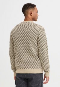 Jersey de punto beige con un patrón texturizado en marrón oscuro, puños y dobladillo acanalados, y cuello redondo. Diseñado para un ajuste relajado.