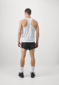 Biały siatkowy top bez rękawów, czarne szorty, czarne buty z logo oraz białe skarpetki typu crew. Podkreślenie sportowego kroju i lekkiego materiału.