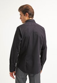 Zwarte lange mouwen shirt met een standaard kraag, een gladde textuur, knoopmanchetten en een getailleerde pasvorm, met een eenvoudige uitstraling zonder patronen.