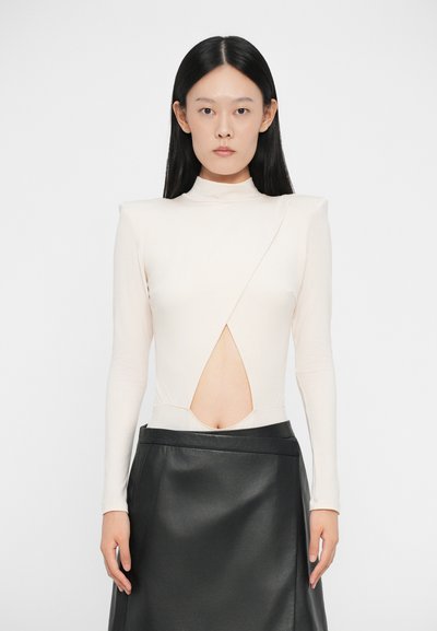 Haut créme à manches longues avec un col montant et une découpe diagonale à la taille, associé à une jupe en cuir noir avec un léger éclat.