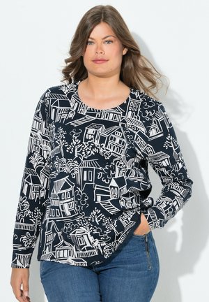 Dlouhý rukáv top vyrobený z tmavě modré látky s bílým vzorem domů a stromů. Zaoblený výstřih, uvolněný střih, lehká struktura a rovný lem.