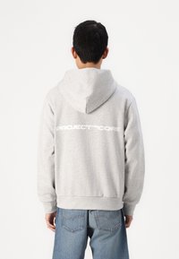 Haut à capuche gris avec cordon de serrage, arborant un grand logo blanc "PROJECT CORE" dans le dos. Tissu doux, coupe décontractée.