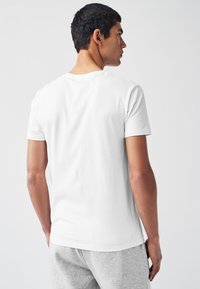 T-shirt bianca a maniche corte in cotone, con scollo rotondo e texture liscia. Il modello è mostrato di spalle.