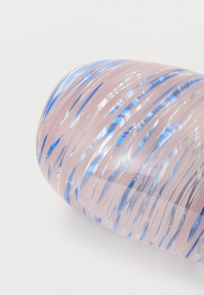 Κοντινό πλάνο ενός διαφανούς γυάλινου αντικειμένου με ροζ και μπλε στροβιλιζόμενες ρίγες πάνω σε λευκή επιφάνεια.
