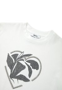 Camiseta de algodón blanca con un diseño floral negro hecho de strass, con un corazón contorneado en cristales. Etiqueta visible en el escote.