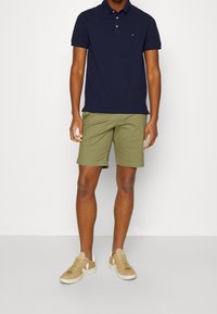 Polo navy, pantalones cortos verde oliva y zapatillas beige. La polo tiene cuello y un pequeño logo, mientras que los pantalones cortos tienen un diseño de frente plano.