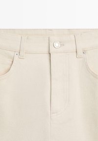 Pantaloni in denim beige chiaro con chiusura frontale a bottoni, passanti per cintura e tasche frontali visibili in primo piano.