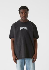Sort oversized t-shirt i denimstof med rund halsudskæring, med hvid grafisk tekst på tværs af brystet og korte ærmer.