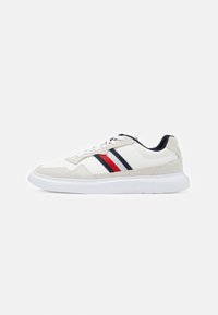 Sneaker bianco con dettagli beige e blu navy, caratterizzato da tre strisce orizzontali in rosso, bianco e blu navy. Suola in gomma, design con lacci, materiali testurizzati.