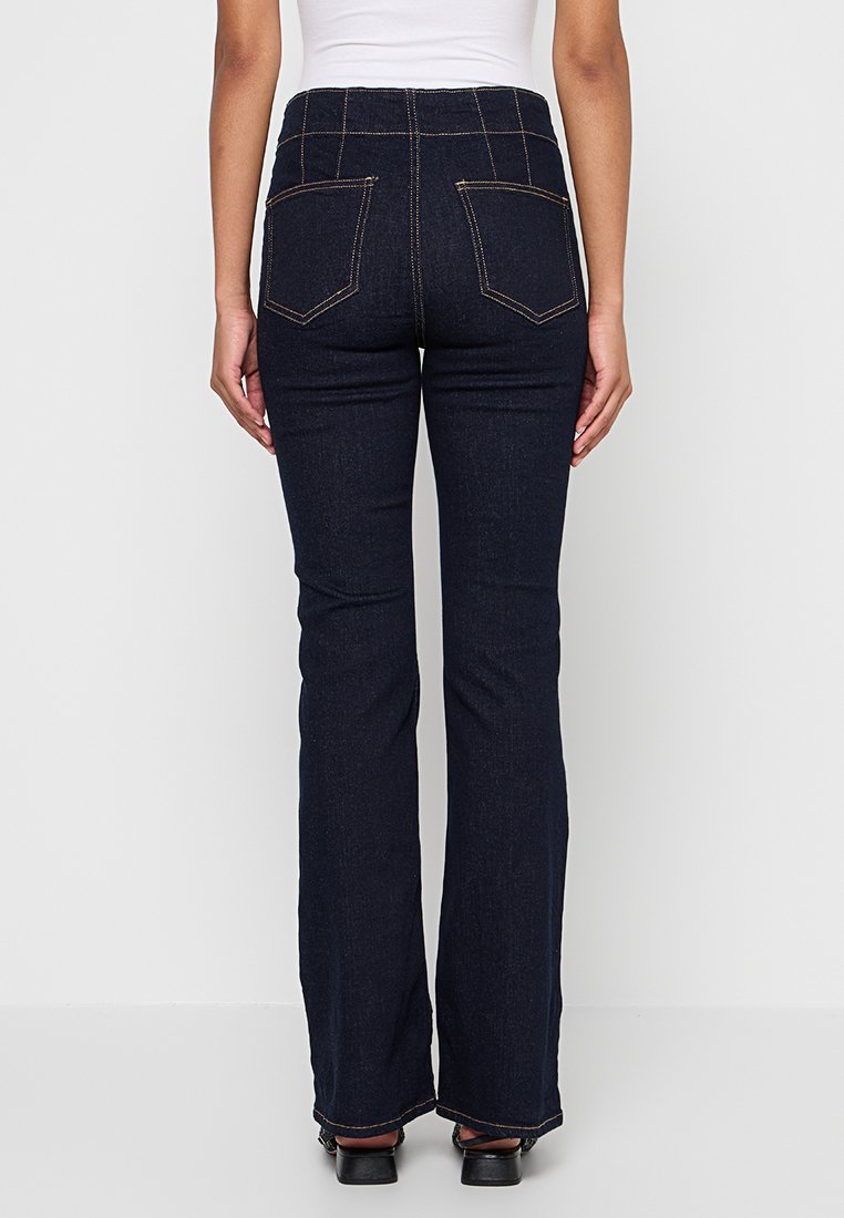 Jeans évasés bleu marine à taille haute, avec des coutures contrastées et deux poches arrière, en tissu denim.