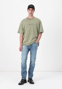 Olive green oversized t-shirt with "HUGO" logo, paired with light blue denim jeans and black leather shoes. Simple design and relaxed fit.