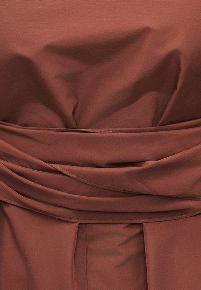 Καφέ ύφασμα με ραμμένες ραφές και στρωματοποιημένα πτυχώματα, πιθανώς μέρος της μέσης ή της ζώνης ενός ενδύματος.