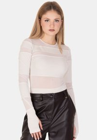 Maglia a maniche lunghe color beige chiaro con righe orizzontali trasparenti, realizzata in un tessuto elasticizzato. Presenta un design aderente e polsini con foro per il pollice.