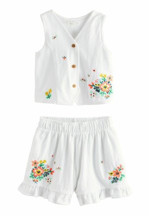 Ensemble blanc à deux pièces composé d'un top sans manches avec des boutons en bois et des broderies florales, et de shorts à ourlet volanté avec des ornements assortis.