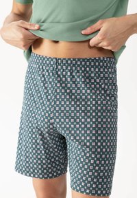 Boxer shorts with a dark green base featuring a repeating pattern of red and white flowers, elastic waistband, and soft fabric texture.