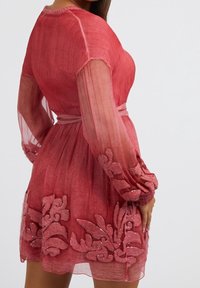 Robe rose transparente à manches longues, avec une broderie florale à l'ourlet et une ceinture en tissu. Tissu texturé avec des variations de couleur subtiles.