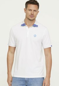 Witte polo met een blauw en rood gestreept kraag, korte mouwen met vergelijkbare accenten en een lichtblauw logo op de borst.