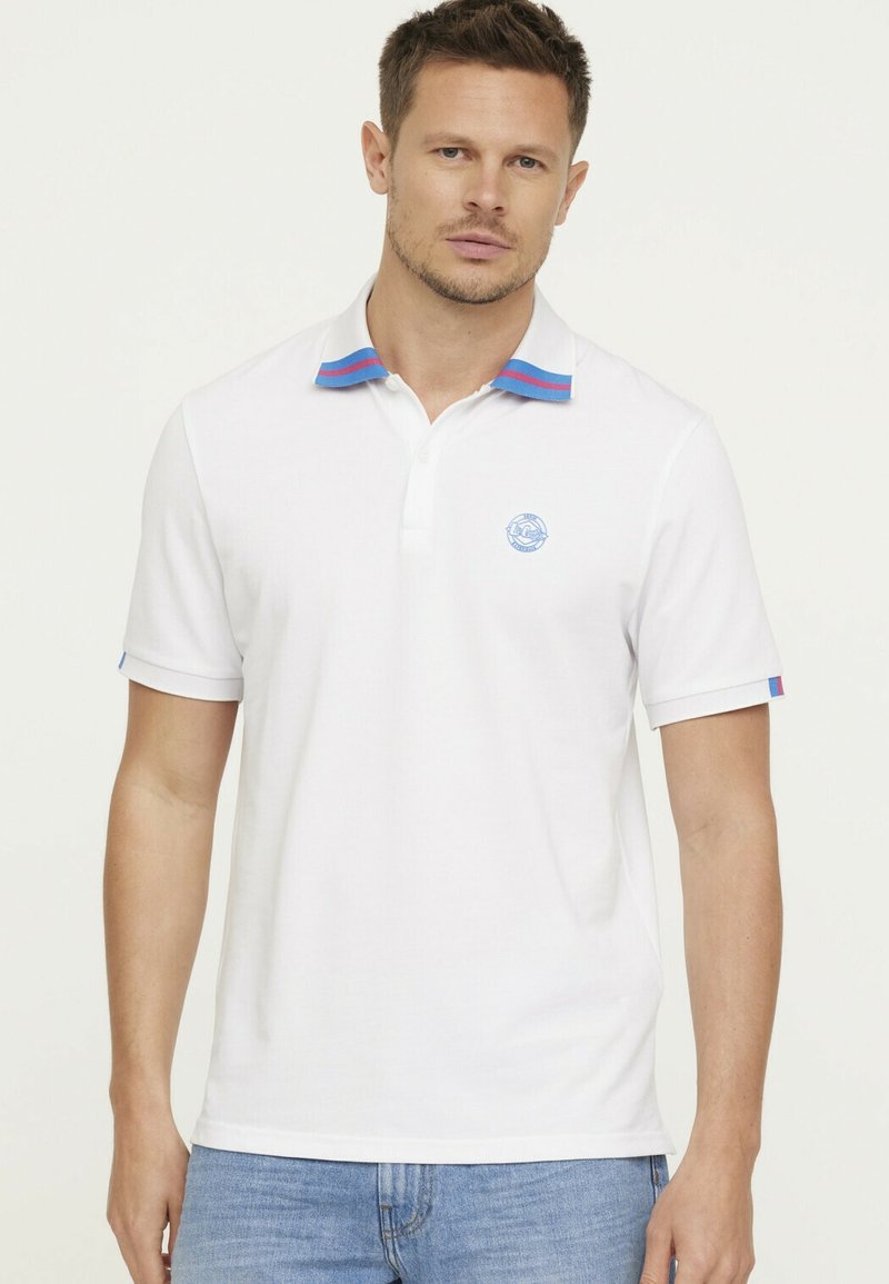 Witte polo met een blauw en rood gestreept kraag, korte mouwen met vergelijkbare accenten en een lichtblauw logo op de borst.