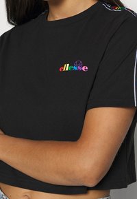 Camiseta negra corta de algodón, con un logo "ellesse" multicolor en el pecho y detalle de rayas de contraste en las mangas.