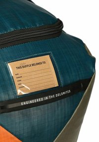 Borsa duffle con un'esterno blu testurizzato, accenti arancioni, una tasca trasparente per l'etichetta del nome e una tracolla nera con la scritta "ENGINEERED IN THE DOLOMITES."