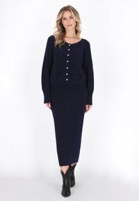Granatowy sweter dziany z okrągłym dekoltem, zapinany na guziki z przodu, z długimi rękawami, zestawiony z dopasowaną, prążkowaną spódnicą midi. Teksturowany materiał.