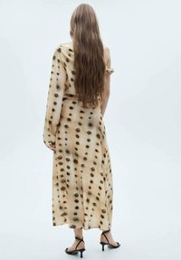 Rochie lungă, cu un umăr, realizată dintr-un material ușor în nuanța bej, cu un model cu pete. Prezintă o siluetă fluidă și un detaliu de dantelare subtilă.