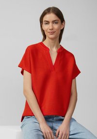 Rood gestructureerd T-shirt met korte mouwen en een V-hals, gecombineerd met lichtblauwe jeans. De stof heeft een geribd patroon.