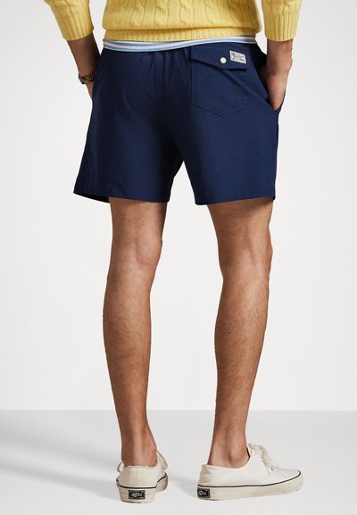 Tamsiai mėlyni šortai, pagaminti iš lygios tekstūros audinio, turintys užpakalinę kišenę su mygtuku ir kontrastingą dryžuotą juosmenį.