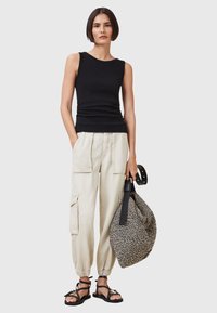 Zwarte mouwloze top, crèmekleurige cargobroek met zijzakken, zwarte sandalen met bandjes, en een tas met een textuur in zwart-wit patroon met een zwarte handgreep.