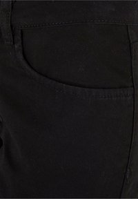 Gros plan sur un tissu en denim noir avec des coutures visibles et une couture de poche incurvée sur un pantalon.
