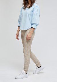 Světle modrá volná blůza s nafouknutými rukávy, spárovaná s béžovými legínami s kostkovaným vzorem a bílými teniskami, předváděná modelem.