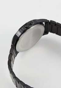 Zwart metalen wristwatch met een gladde ronde kast, gepolijste accenten en een schakelarmband. Heeft een kroon aan de rechterzijde en een zilveren achterkant.