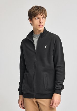 Sort zip-up sweatshirt med høj krave, sidelommer og et lille hvidt logo på brystet. Stoffet ser glat ud med en afslappet pasform.