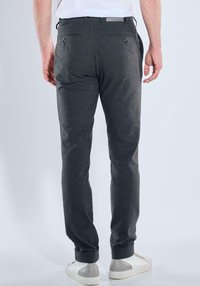 Grau maßgeschneiderte Hose aus glattem Stoff mit schmal zulaufender Passform, ausgestattet mit Gesäßtaschen und umgeschlagenen Säumen, kombiniert mit weißen Sneakern.