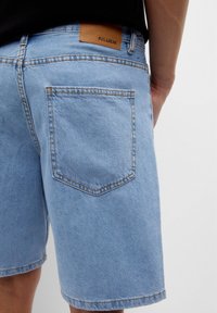 Svetle modré denimové šortky se standardním střihem, které mají zadní kapsu a koženou nášivku s nápisem "PULL&BEAR" na pase.