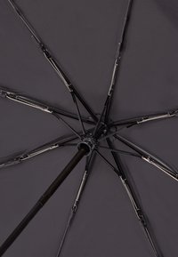 Black umbrella viewed from below, featuring metallic ribs, a central pole, and a circular canopy with a smooth texture.