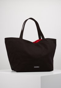 Czarna torba na ramię z płótna z czerwoną podszewką, zawierająca dwa mocne uchwyty i minimalistyczny design. Ozdobiona naszywką z logo.