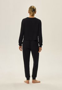 Czarny zestaw dresowy z prążkowanej tkaniny składa się z krótkiej bluzki z długim rękawem oraz tapered spodni z elastycznymi mankietami. Minimalistyczny design, miękka tekstura.