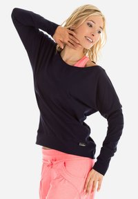 Granatowy longsleeve z szerokim dekoltem i długimi rękawami, w połączeniu z różowymi dresami z kieszeniami po bokach i sznurkiem w talii. Miękka tekstura.