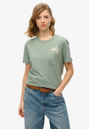 Camiseta de algodón verde claro con un bolsillo y un gráfico de nube con luna. Combinada con unos vaqueros de mezclilla azul de cintura alta, ligeramente sueltos, y un cinturón marrón.
